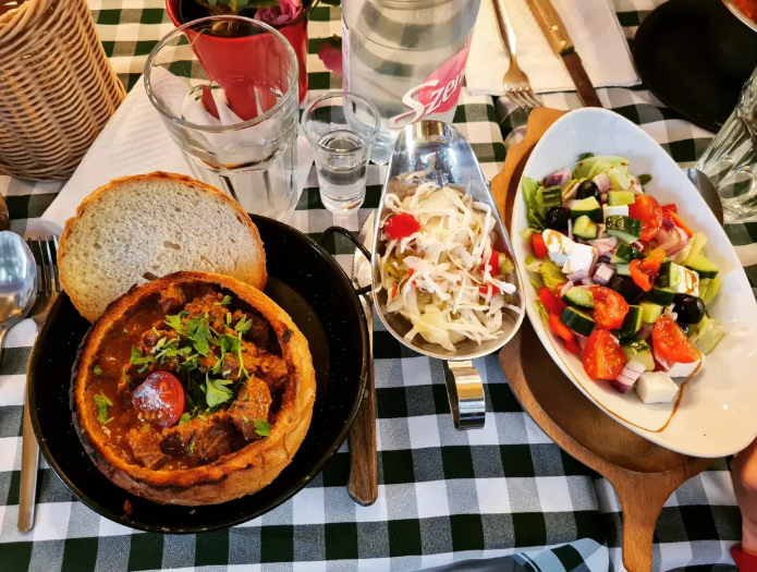 Goulasch hongrois dans un bol de pain accompagné d'une salade de crudités à la grecque.